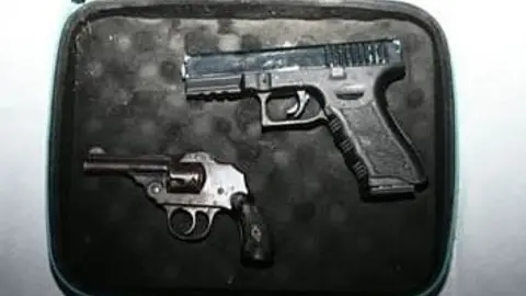 Two guns - a Glock-style pistol and a small vintage-looking enclosed-hammer revolver - lie in a small case which has black padding.