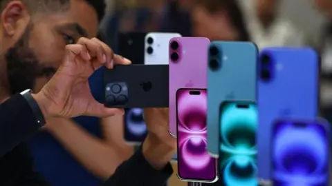 Getty Images Man looking at iphones that are on display in a range of blue green and purple colours