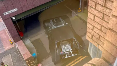 The Batmobile - a souped up black car - driving into a car park.
