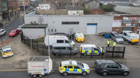 PA A number of police cars and vans are surrounding a large grey warehouse which has the sign saying Legacy on its wall