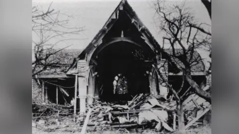 All Saints Church, South Merstham A black and white image of a destroyed church building. The front of the building is caved in with rubble strewn around it.