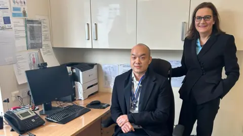 NHS Essex ICB Dr Andy Huynh and Rebecca Harris by a desk inside the new surgery.