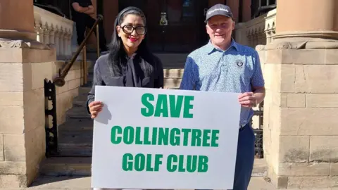 Nadia Lincoln/LDRS A woman and a man hold up a white sign with "Save Collingtree Golf Club" written in green letters. 