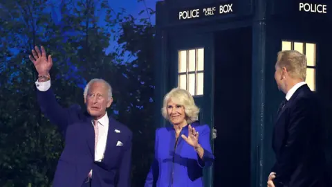 King Charles III and Queen Camilla emerge from a Tardis at the Commonwealth Games opening ceremony and wave, as a kilted Sir Chris Hoy greets them