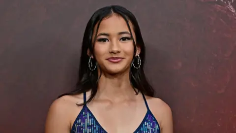 Kaylee Hottle wears a blue and purple sparkly dress and silve hoop earrings. 