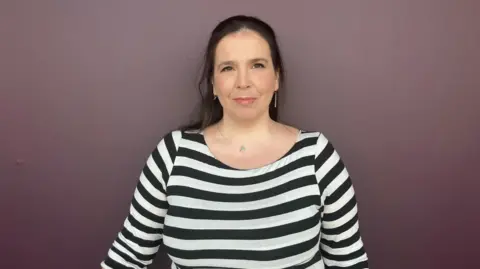 BBC Laura Murtagh - a woman with shoulder length dark hair and wearing a black and white striped top - looks directly into the camera.