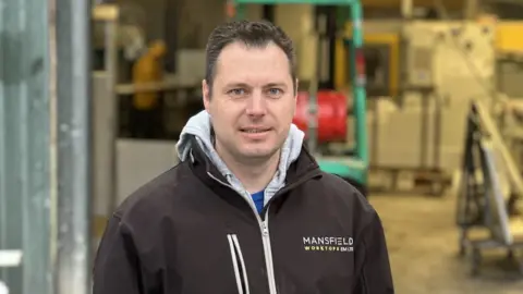 Ashley Barnes, who runs Mansfield Worktops, dressed in a logoed jacket, looking at the camera with his premises in the background