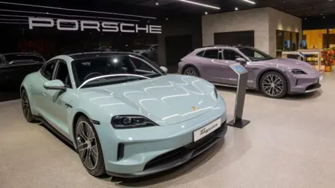 Getty Images A pair of Porsche Taycan electric cars, one in pastel blue and another in lilac, are parked side-by-side in a showroom in Hong Kong