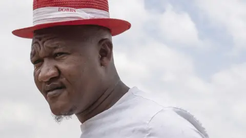 A head shot of man in a red hat looks to the left of the camera.