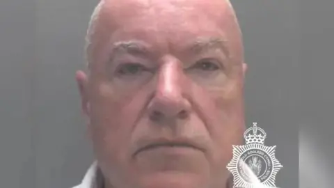 North Wales Police A mugshot of Neil Foden. He is a bald, white man and is looking at the camera. On the bottom right of the image is a North Wales Police logo.
