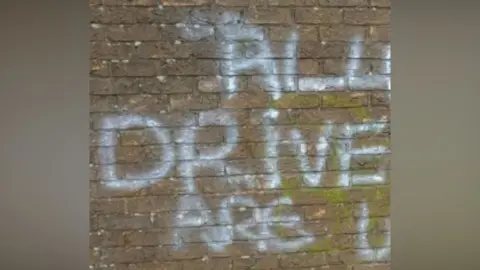 North Yorkshire Police A section of brick wall with graffiti daubed on it in white paint. Only the words "all drive are u" are visible as the image has been cropped.
