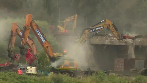 bbc A bulldozers crashes into the bridge as it demolishes it