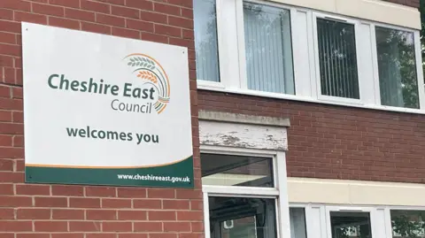 Cheshire East Council's headquarters at Delamere House in Crewe. There is a sign on the building that says Cheshire East Council welcomes you.