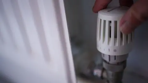 A hand adjusting the thermostat attached to a white radiator.
