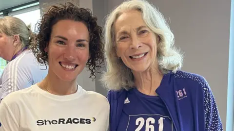 Kathrine Switzer y Sophie Power Sophie Power a la izquierda con una camiseta blanca que dice "Ella corre" y Kathrine Switzer a la derecha con un top morado con "261" en él.