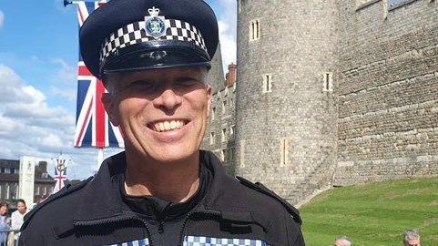 Nick Reuter wearing a police uniform with a cap and standing in front of Windsor Castle