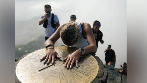 Woman rests hands on mountain top marker
