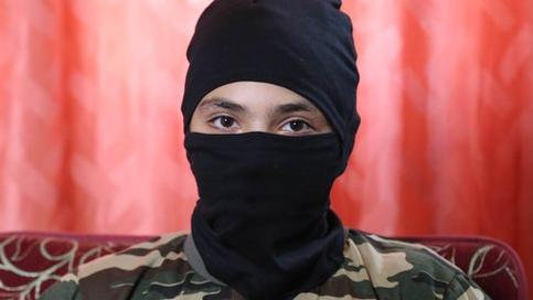 A 13-year-old boy who wishes to be named 'Abu Hattab' sits wearing a black balaclava