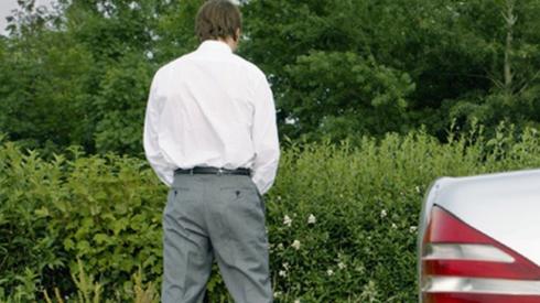 Stock photo of a man urinating at the side of the road