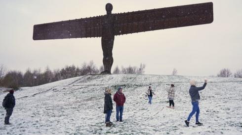 People play in snow around Angel of the north