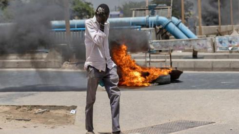 A man wipes his eyes as he walks past burning tyres near Cheikh Anta Diop University in Dakar, Senegal - 1 June 2023