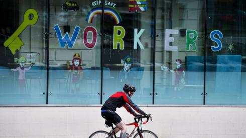Man on bike driving past workers sign
