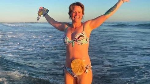 Gill standing in the sea in a bikini with her arms held high and her colostomy bag visible