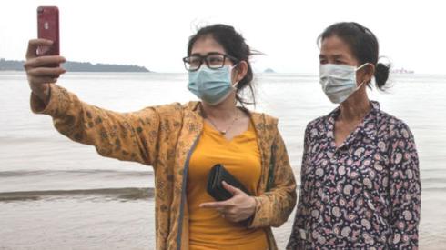 Two women in masks take a selfie on a beach