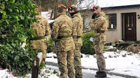 Army troops in the snow outside a house