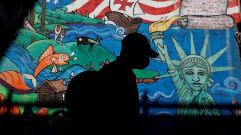 A man in a mask walks in front of a mural in New York