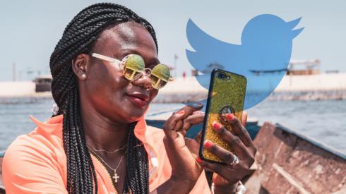 A woman in Ghana using a phone with the Twitter logo in the background