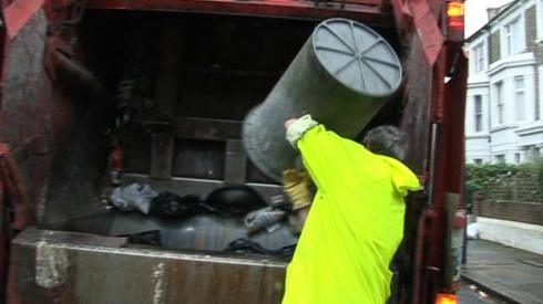 Binman tips rubbish bin and deposits refuse into back of refuse truck in Hammersmith