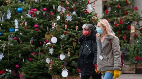 Two people wearing face masks by Christmas trees