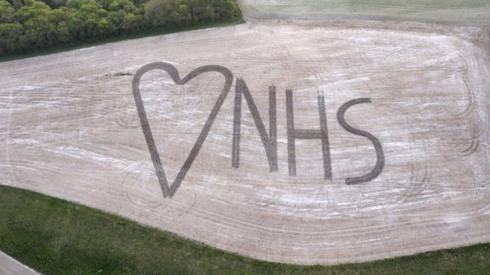 An aerial view on to a field in which NHS and a heart sign has been marked out using crops