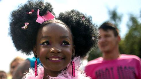 A young girl wearing a pink feather boa and matching earrings and hair bows takes part in the march.