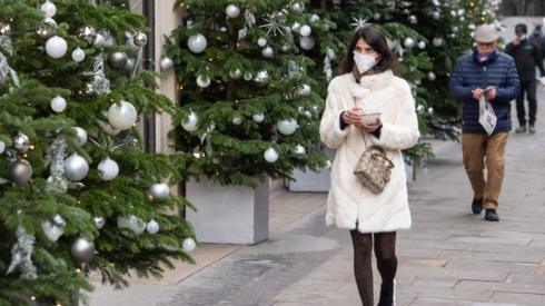 A woman wearing a face mask walks passes a display of Christmas trees outside a shop in central London,