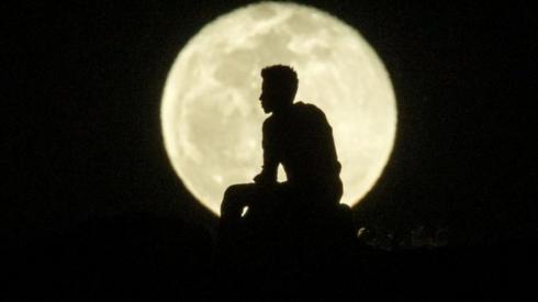 A man's silhouette is seen against a bright, full moon.