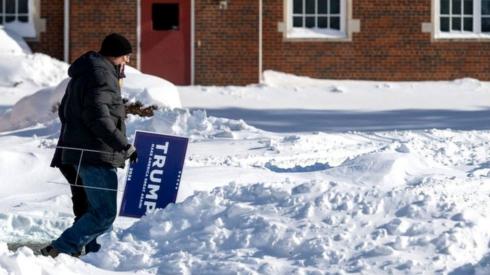 A man carries in Trump sign in the snow in Iowa