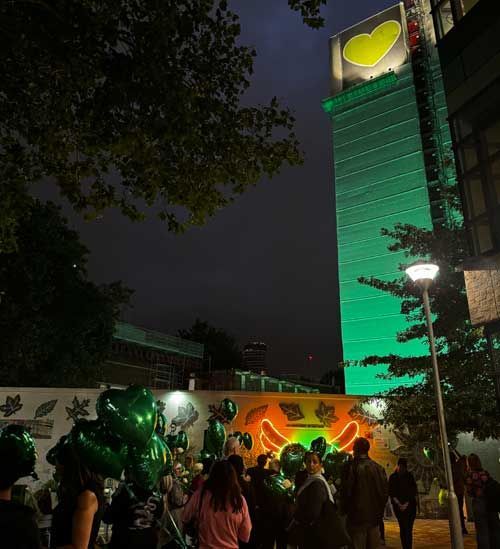 An image of the Grenfell Tower lit up in green against the backdrop of a night sky in London on Wednesday night, with people gathered at the base