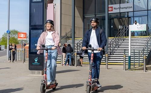 A man and a woman on e-scooters outside Northampton railway station