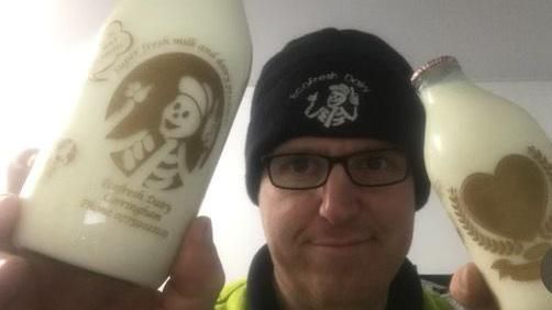 Paul Luke, wearing a hat and glasses, holding two bottles of milk