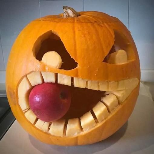 Carved pumpkin of a scary face with an apple in its mouth