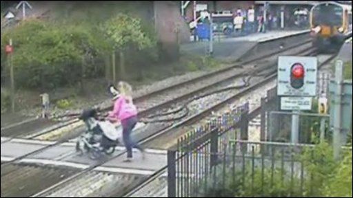 A woman running across a railway line with a pram in front of an approaching train