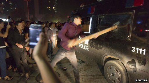 A man breaks the window of a police van with a wooden plank during a protest in Yuyao