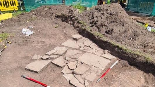 Mounds of mud and dirt at an excavation site. Two long red and white poles at either end of the site