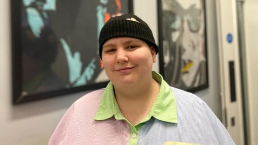 Rhyen smiling at the camera, wearing a black beanie hat and a multicoloured shirt