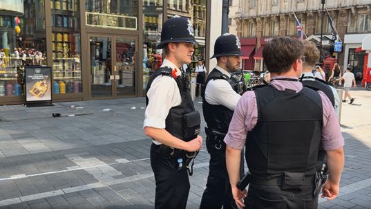 Two uniformed police officers talk to two plain clothes officers by the crime scene cordon in Leicester Square