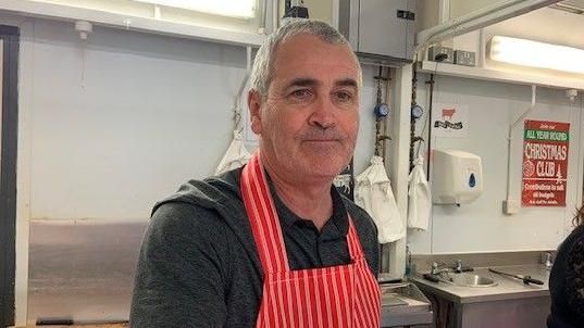 Bill Ferguson is wearing a traditional butcher's apron and has a neutral expression