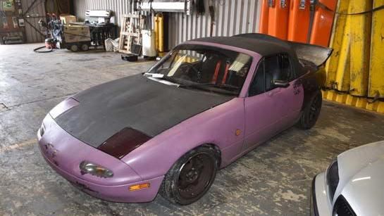 A purple and black Mazda MX-5 parked in a garage