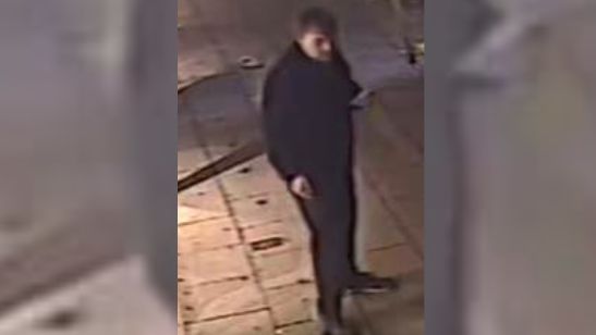 A still of a man, standing outside on a pavement, taken from CCTV footage